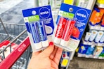 person holding 2 nivea lip balm 2-packs by a cvs cart