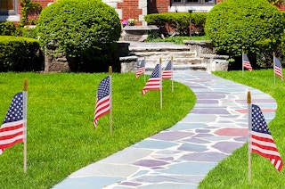 Mini American flags stuck in the ground along a stone path.