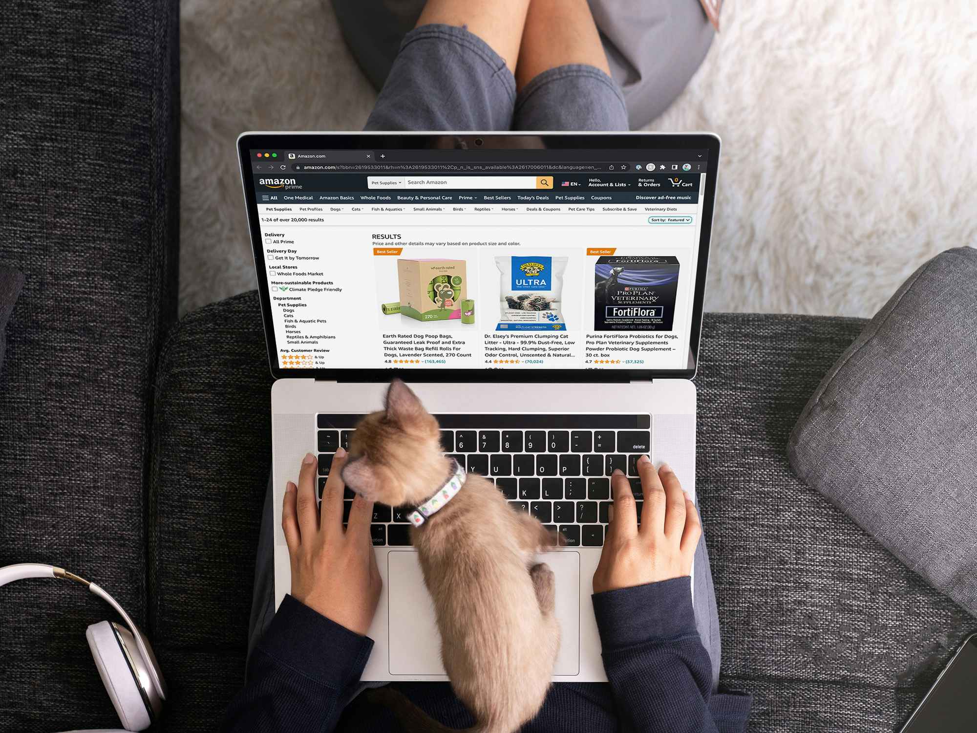 A person looking at pet deals on Amazon using a laptop while a kitten is trying to step on the keyboard
