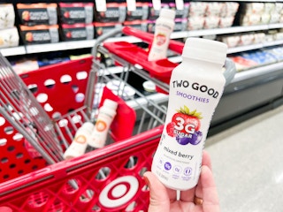 hand holding bottle of Two Good Smoothie in front shopping cart
