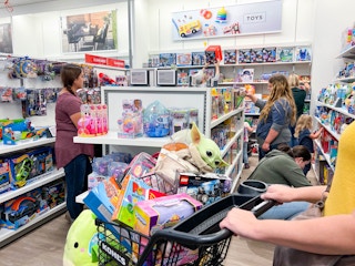 A woman pushing a kohl's cart filled with toys in a busy toy aisle.-kcl-model