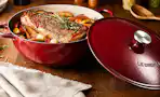 Lifestyle image of a red Le Creuset 5.25-qt Traditional Cast Iron Chef's Oven with food cooked inside