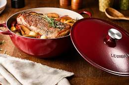 Lifestyle image of a red Le Creuset 5.25-qt Traditional Cast Iron Chef's Oven with food cooked inside 
