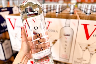 a person holding up a bottle of kirkland vodka 