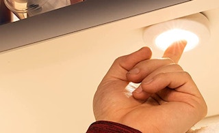 A finger turning on the tap light in a cabinet