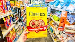 person holding a box of cheerios in an aisle