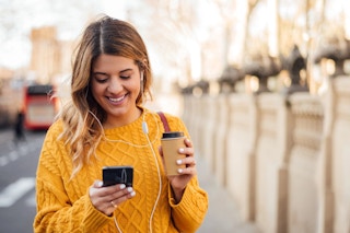 A woman in a yellow sweater smiles at her phone
