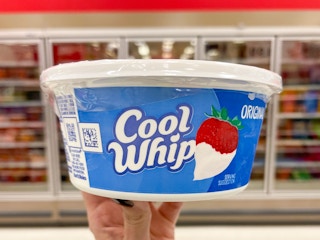 A container of Cool Whip held up by hand in front of a refrigerating section.