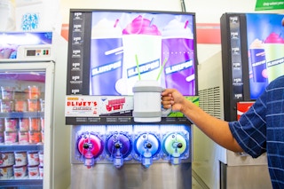 Hand holding a large cup with slurpee machine in the background