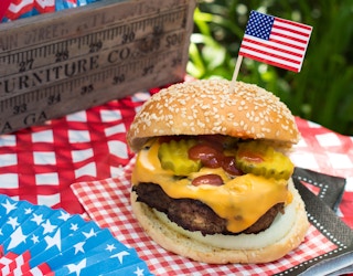 A large hamburger on a table with some Americana decor and a small American flag toothpick in the bun