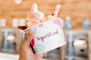 Person holding cup of yogurt in front of yogurt machines.