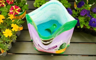 an open bag of blue flower food next to flowers outside