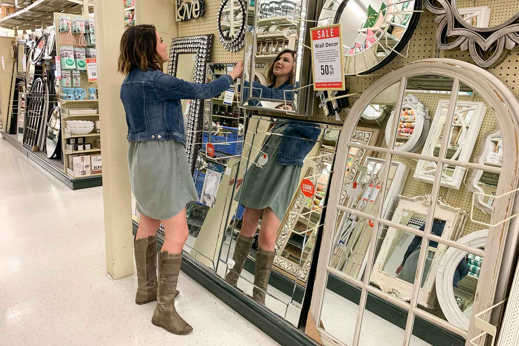 A woman looking at a mirror in an aisle filled with mirrors of varying styles and sizes at Hobby Lobby.