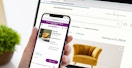 person comparing yellow anthropologie chair with similar chair on wayfair with iphone and laptop