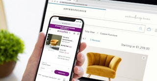 person comparing yellow anthropologie chair with similar chair on wayfair with iphone and laptop