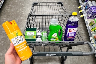 hand holding disinfectant spray in front of shopping cart filled with cleaning supplies