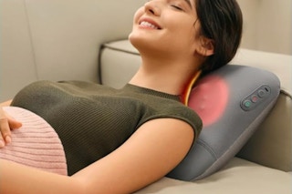 Woman laying on a couch using the SKG Cordless Back Massager.