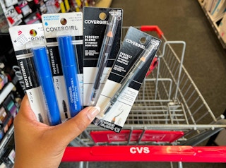 hand holding two Covergirl mascaras and one Covergirl eyeliner