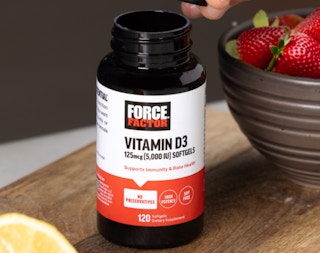 a bottle of vitamins sitting on a table next to a bowl of strawberries