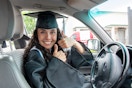 Woman in a graduation cap and gown sitting behind the wheel of a car.