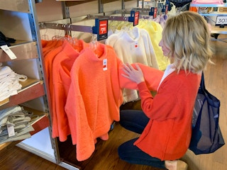 A woman looking at a bright coral colored sweater with a sale sign above.