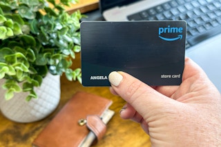 an amazon store card being held in front of wallet and computer 