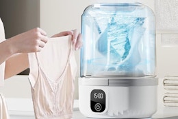 a woman holding a top near a mini washing machine