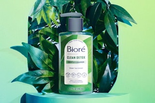 a bottle of cleanser on a green display in front of leaves