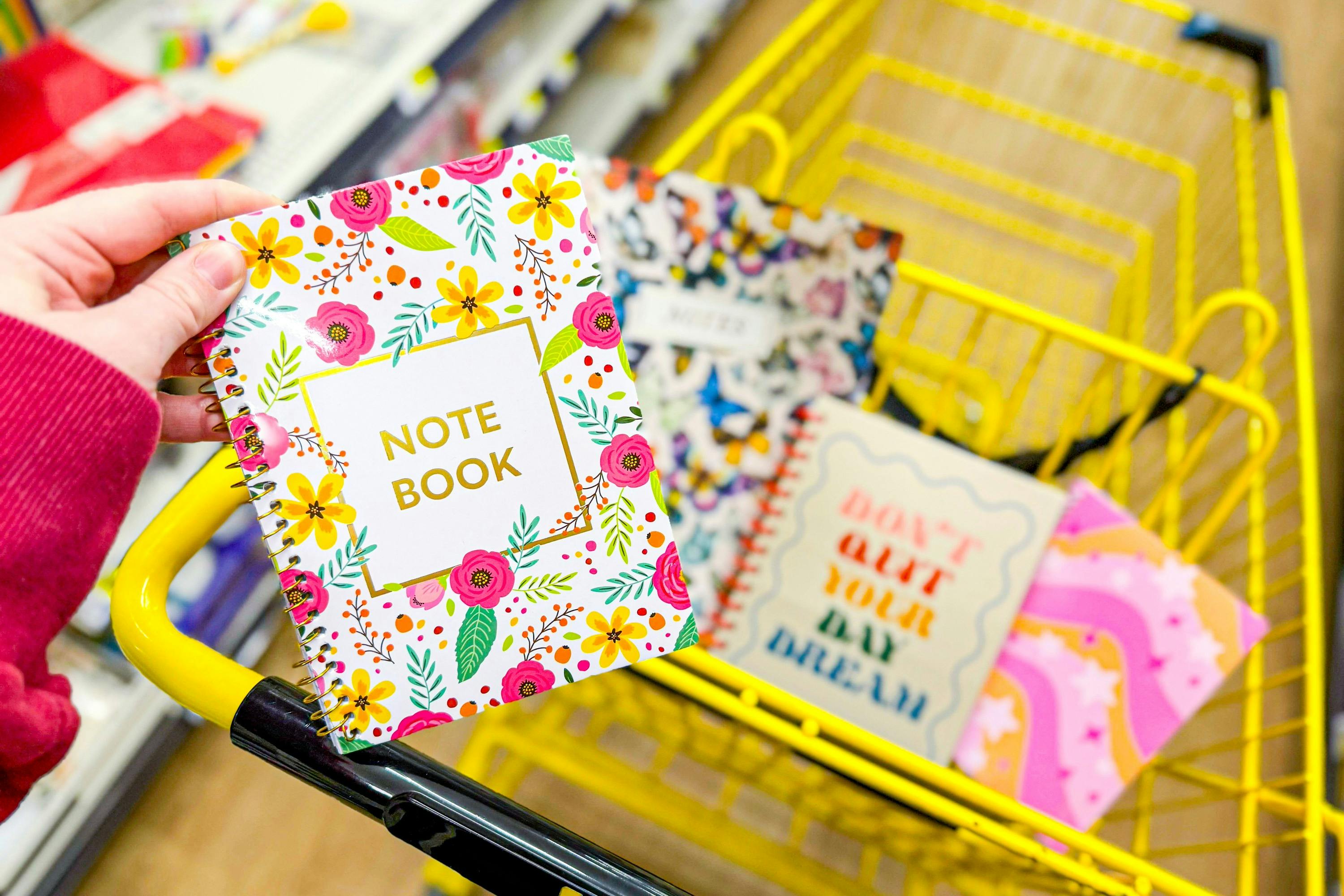hand holding a journal above a yellow shopping cart full of journals