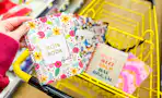 hand holding a journal above a yellow shopping cart full of journals
