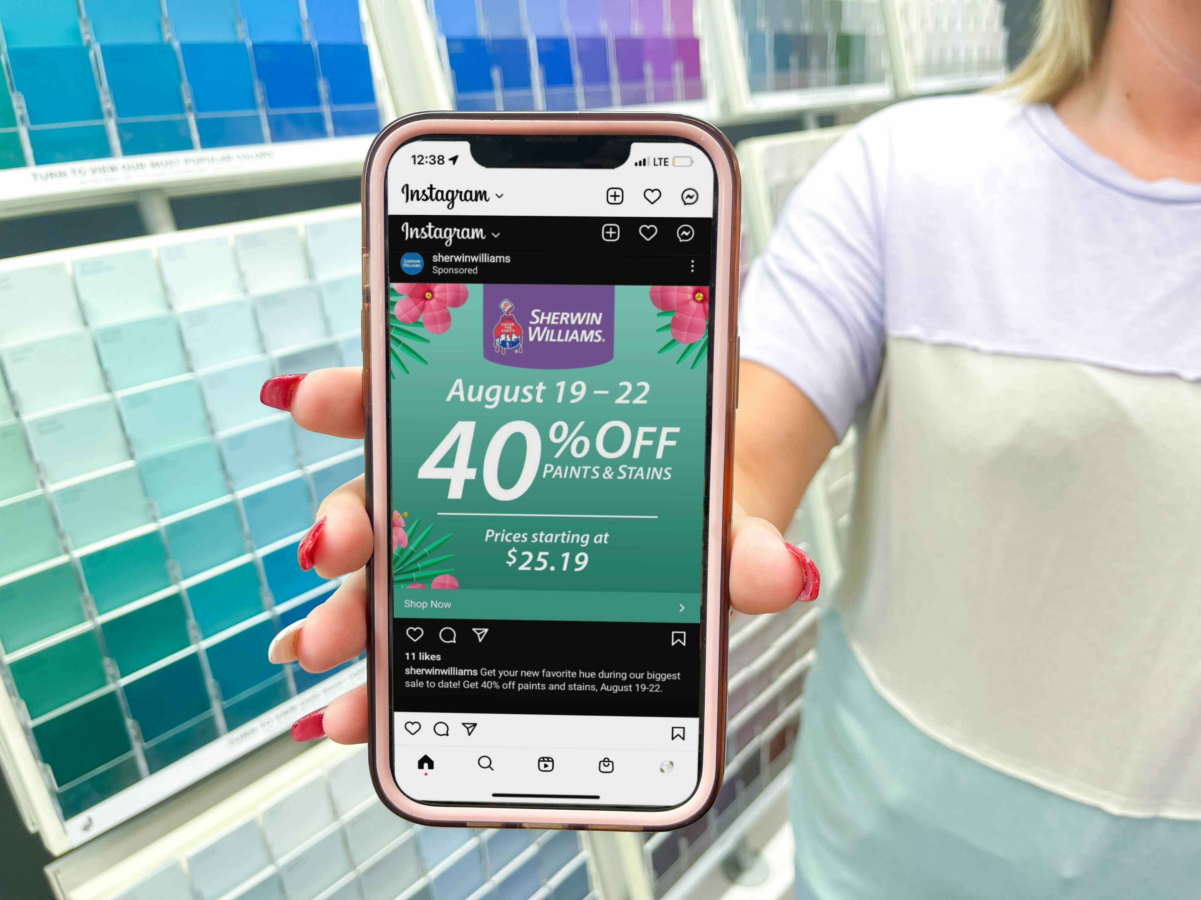 cellphone being held in front of paint swatch color wall with sherwin williams instagram coupon on screen