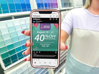 cellphone being held in front of paint swatch color wall with sherwin williams instagram coupon on screen