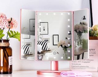 A tri-fold lighted makeup mirror near flowers and a towel.