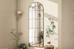 Lifestyle image of an arched full length windowpane mirror hung on wall
