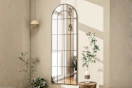 Lifestyle image of an arched full length windowpane mirror hung on wall