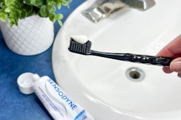 a person holding a toothbrush with toothpaste over a sink with a tube of toothbrush