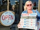 a woman holding a stack of pizza boxes outside dominos