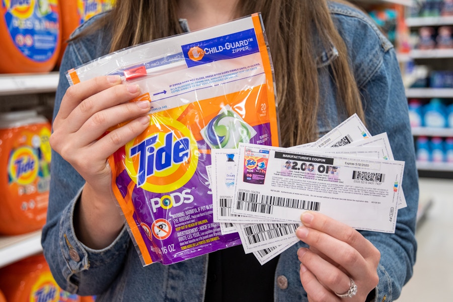 A woman holding a pack of tide Pods with printed manufacture coupons in hand.