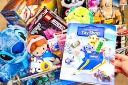 The 2025 Walmart toy shop catalog book being held in store next to a cart full of top toys. 