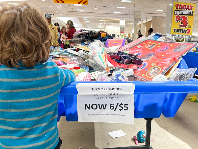 A child looking through a bin with a sign that says "now 3/$5" in a Turn7 store