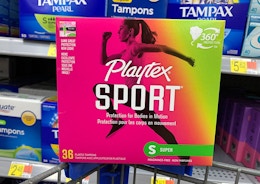 a hand holding a pink and green box of tampons 