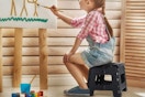 a girl painting while sitting on a step stool
