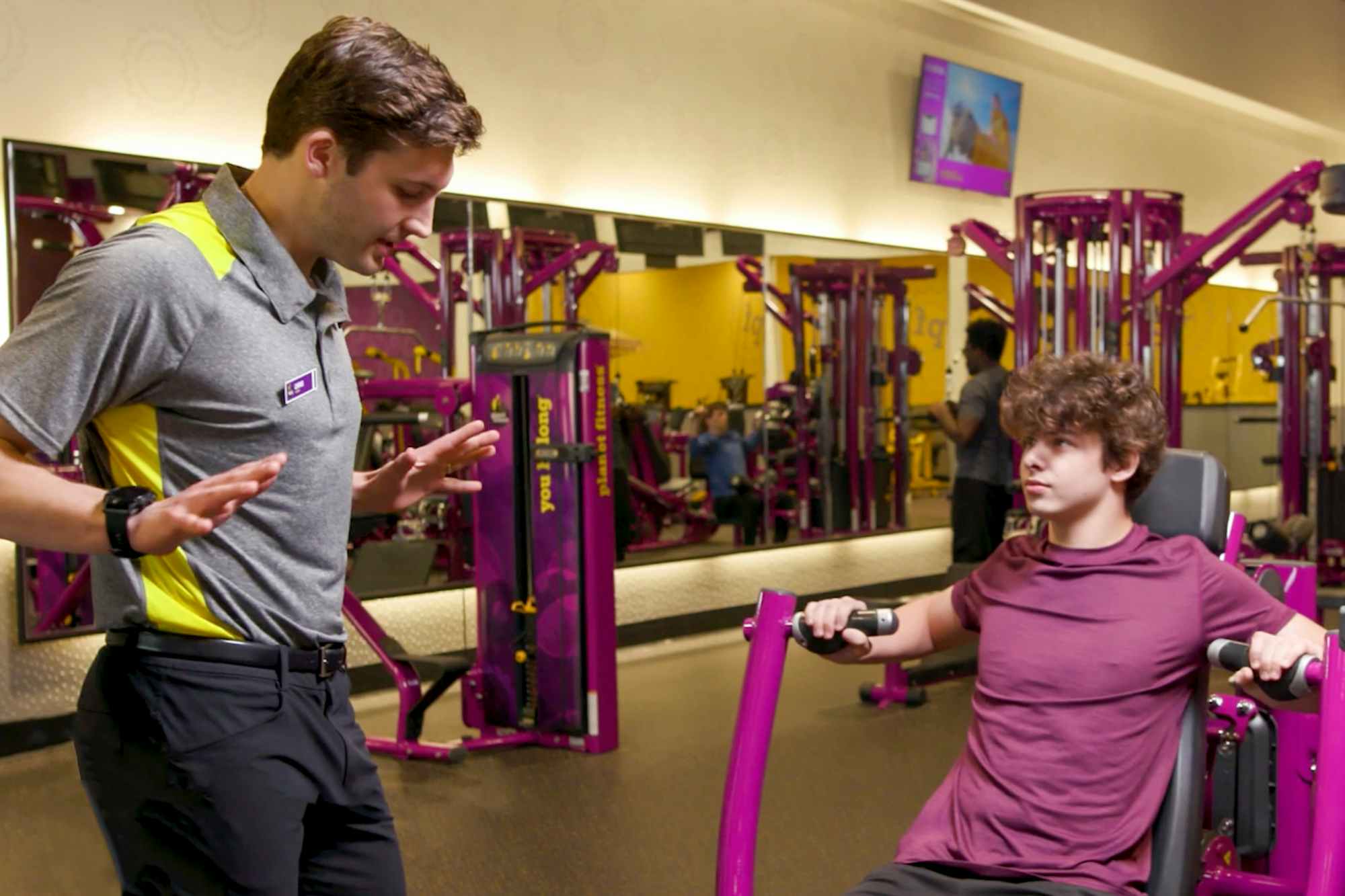 A Planet Fitness trainer showing a teen how to use a machine