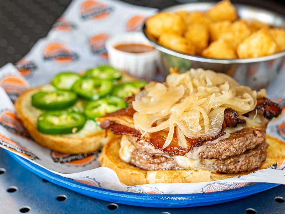 open face burger topped with grilled onions and a side of tater tots