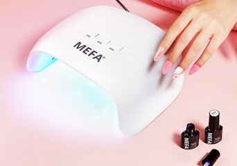 a hand with long nails on a top of a UV nail lamp 