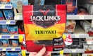A hand holding Jack Link's beef jerky in a store aisle.