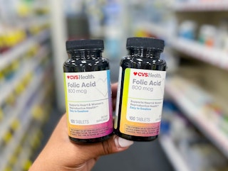 person holding two bottles of CVS Health Folic Acid vitamins in aisle
