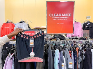 A woman holding a pair of Under Armour shorts next to a clearance sign