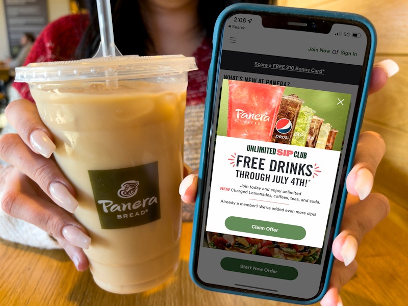 A woman holding an iced coffee in a panera cup next to a cell phone displaying a deal for the unlimited sip club on the panera app.