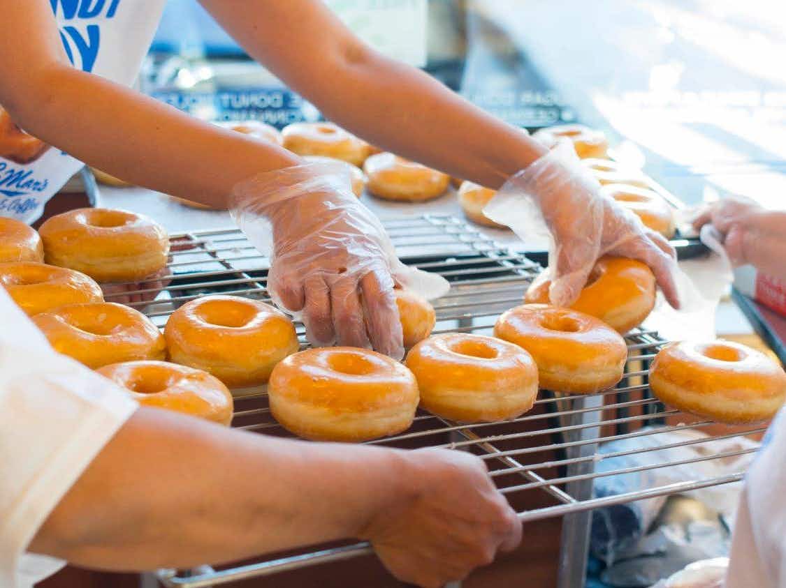 Some LaMar Donuts employees sorting glazed doughnuts on a tray.